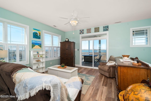 living room with a water view, wood finished floors, visible vents, and a ceiling fan