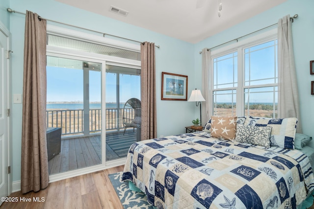 bedroom featuring access to outside, a water view, visible vents, and light wood-style floors