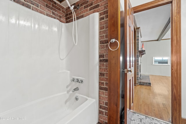 bathroom featuring shower / bathing tub combination, wood-type flooring, and brick wall