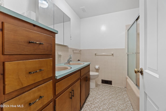 full bathroom featuring tile patterned floors, toilet, shower / bath combination with glass door, vanity, and tile walls