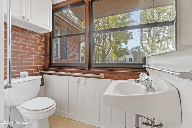 bathroom with sink, toilet, a healthy amount of sunlight, and brick wall