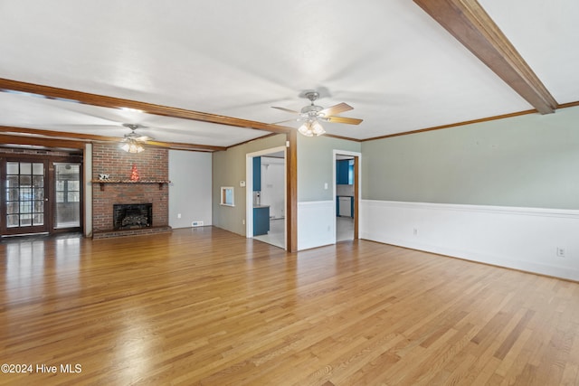 unfurnished living room with light wood-type flooring, a fireplace, ornamental molding, ceiling fan, and beamed ceiling