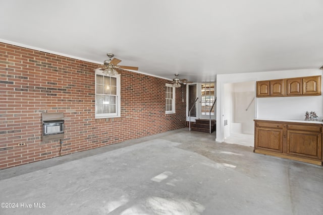 unfurnished living room featuring ceiling fan and brick wall