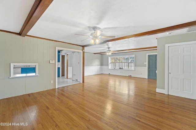 unfurnished living room featuring ceiling fan, wooden walls, crown molding, beam ceiling, and light hardwood / wood-style floors