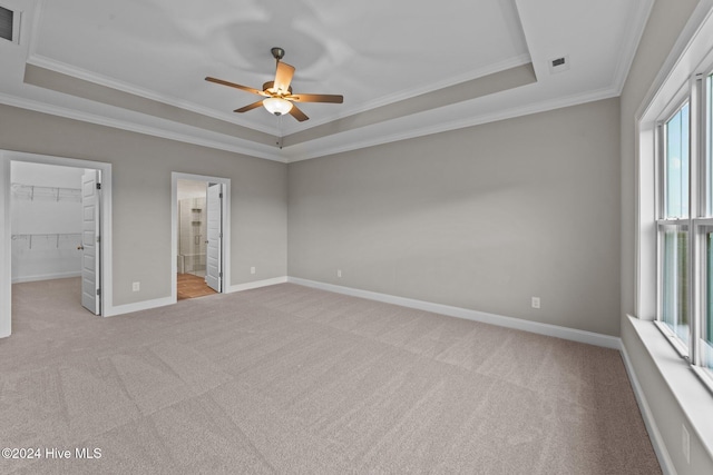 unfurnished bedroom featuring a raised ceiling, a walk in closet, ceiling fan, and ensuite bath