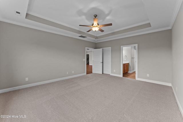 unfurnished bedroom featuring ensuite bath, ceiling fan, light colored carpet, a tray ceiling, and ornamental molding