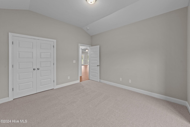 unfurnished bedroom with light colored carpet, lofted ceiling, and a closet