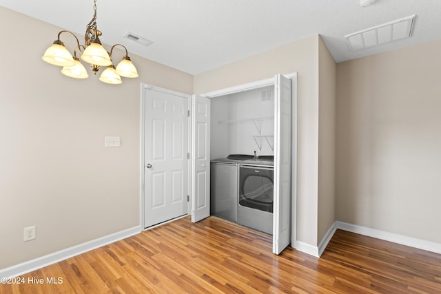 clothes washing area with washer and dryer, hardwood / wood-style floors, and a notable chandelier