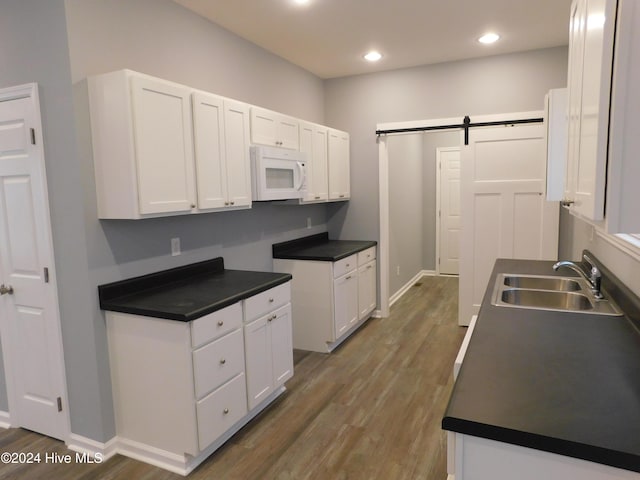 12521 Mckinnon Dr, Laurinburg, NC 28352 - kitchen with white microwave, a barn door, wood finished floors, white cabinets, and recessed lighting