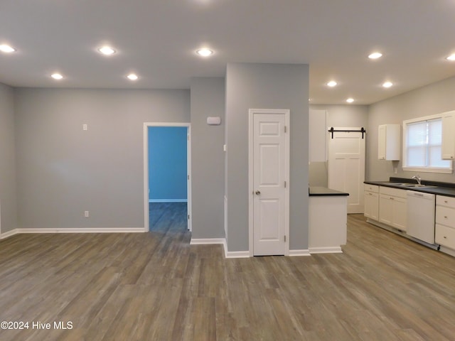 kitchen featuring wood-type flooring, a barn door, white dishwasher, and white cabinetry