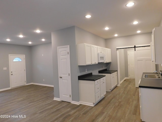 12521 Mckinnon Dr, Laurinburg, NC 28352 - kitchen with a barn door, white microwave, dark wood-type flooring, white cabinetry, and dark countertops