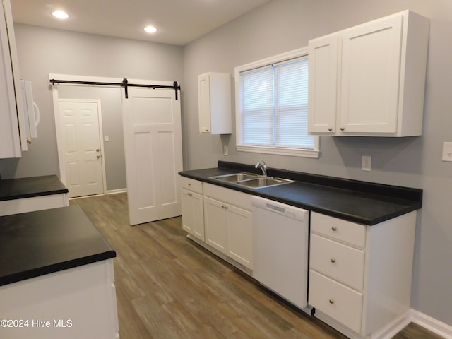 kitchen with white dishwasher, dark wood-type flooring, sink, a barn door, and white cabinetry