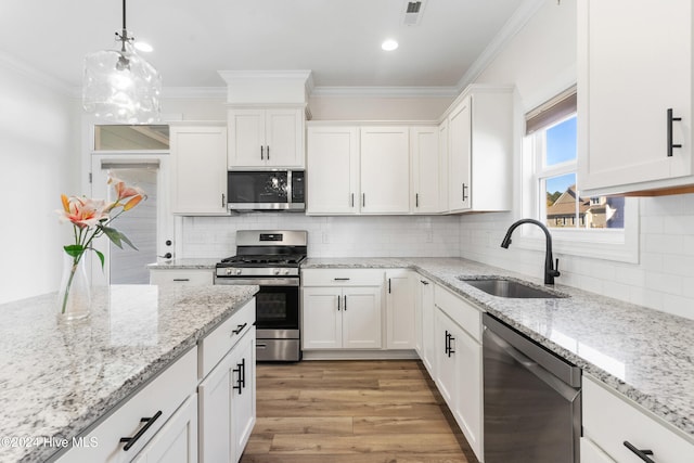 kitchen featuring white cabinetry, sink, hanging light fixtures, stainless steel appliances, and light wood-type flooring