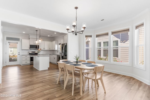 dining room with light wood-type flooring, ornamental molding, and an inviting chandelier