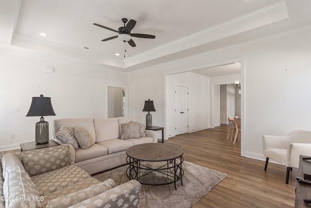 living room with a tray ceiling, ceiling fan, wood-type flooring, and ornamental molding