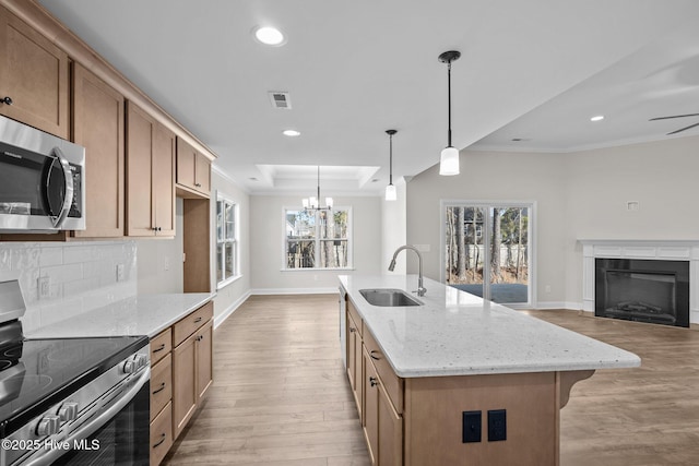 kitchen featuring appliances with stainless steel finishes, a center island with sink, hanging light fixtures, light stone counters, and sink