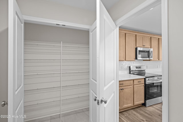 kitchen with appliances with stainless steel finishes, light hardwood / wood-style floors, and backsplash