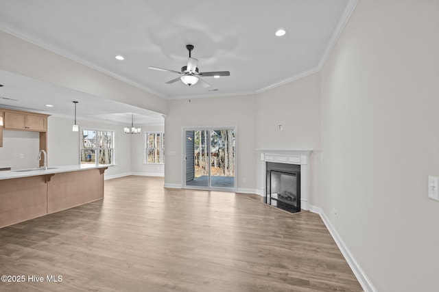 unfurnished living room with ceiling fan with notable chandelier, sink, light wood-type flooring, and crown molding