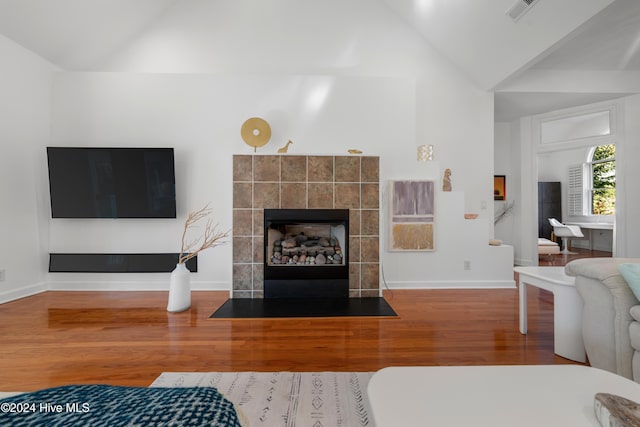 living room featuring high vaulted ceiling, wood-type flooring, and a tile fireplace