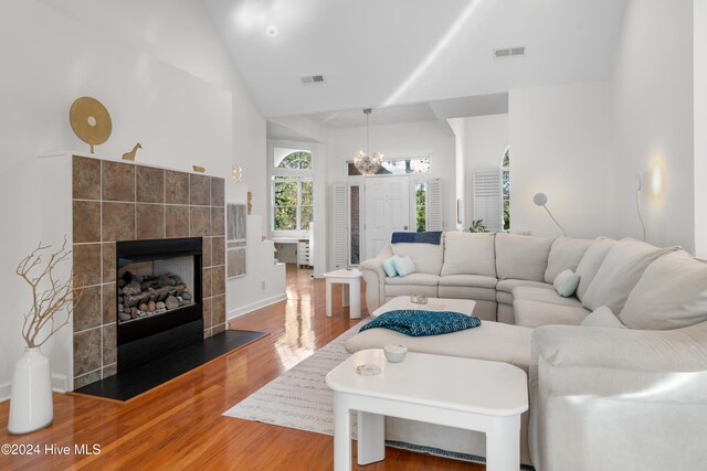 living room with a tile fireplace, hardwood / wood-style flooring, high vaulted ceiling, and a chandelier