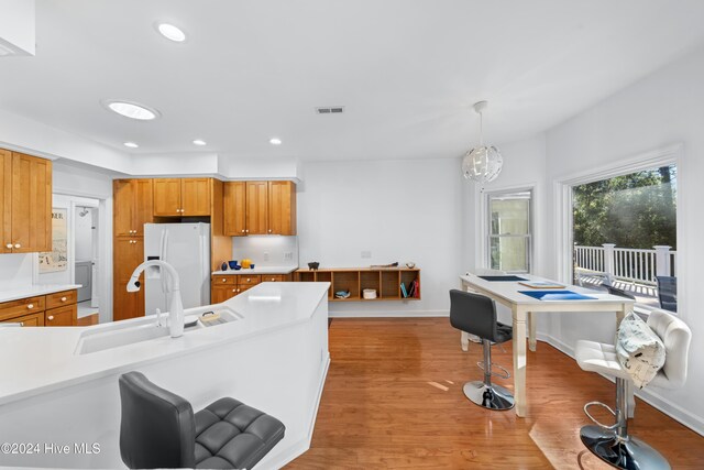 kitchen featuring light wood-type flooring, sink, white fridge with ice dispenser, a chandelier, and hanging light fixtures