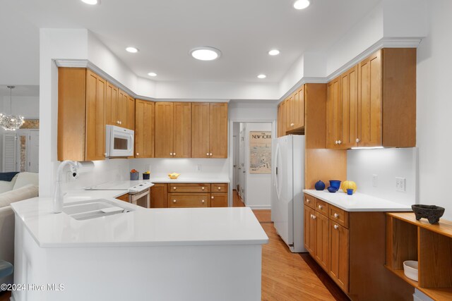 kitchen with sink, kitchen peninsula, a chandelier, light hardwood / wood-style floors, and white appliances