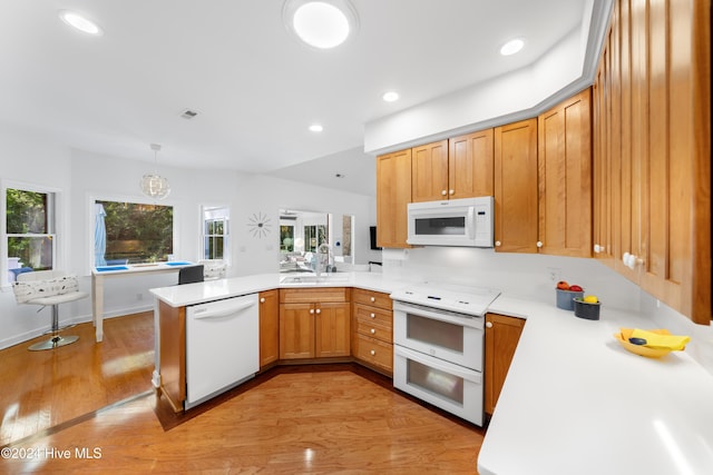 kitchen featuring pendant lighting, white appliances, sink, light hardwood / wood-style floors, and kitchen peninsula