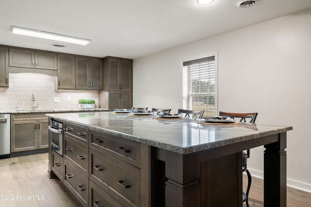 kitchen with a kitchen bar, light stone countertops, sink, light hardwood / wood-style flooring, and a kitchen island