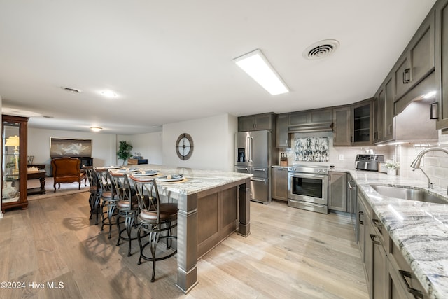 kitchen featuring sink, light hardwood / wood-style flooring, a kitchen island, light stone counters, and stainless steel appliances