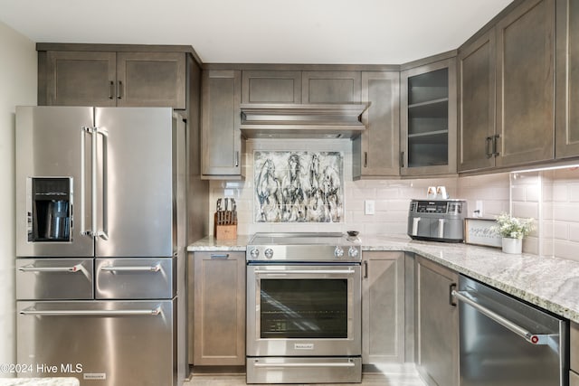 kitchen with light stone countertops, appliances with stainless steel finishes, dark brown cabinetry, and decorative backsplash