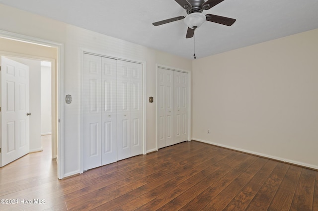 unfurnished bedroom featuring two closets, ceiling fan, and dark wood-type flooring