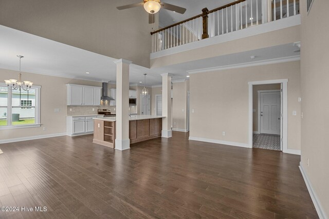 unfurnished living room featuring a towering ceiling, ornamental molding, ceiling fan with notable chandelier, and dark hardwood / wood-style floors