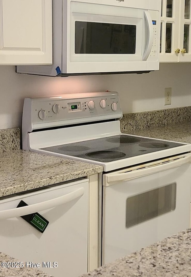 kitchen with white cabinetry, light stone countertops, and white appliances