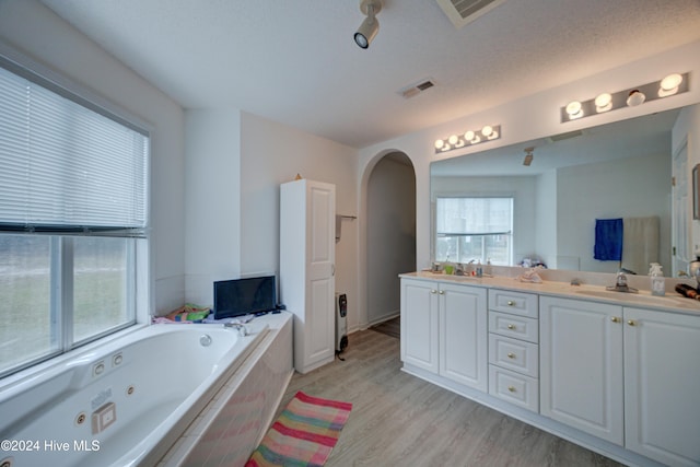 bathroom featuring vanity, hardwood / wood-style floors, a textured ceiling, and tiled tub