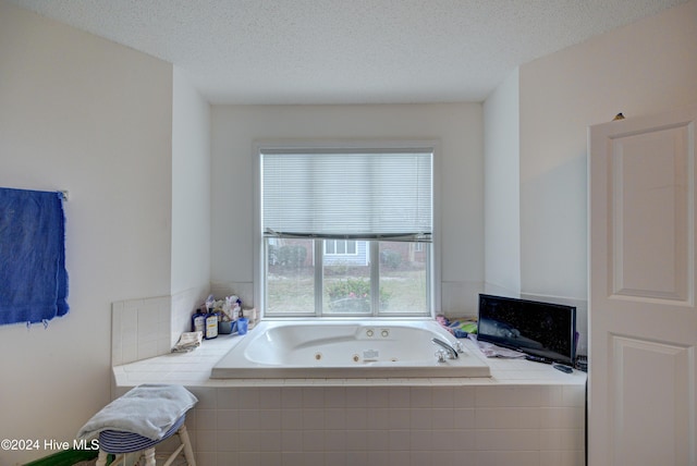 bathroom with a relaxing tiled tub and a textured ceiling