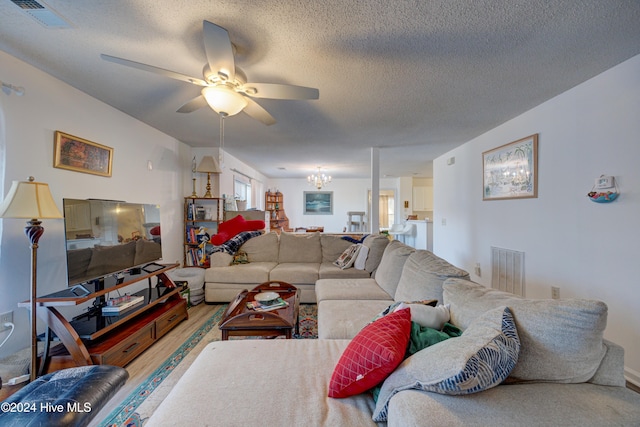 living room featuring ceiling fan with notable chandelier, a textured ceiling, and hardwood / wood-style flooring