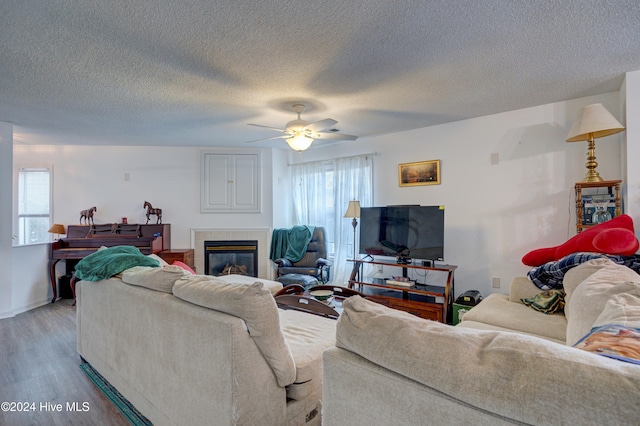 living room featuring ceiling fan, a textured ceiling, a fireplace, and wood-type flooring