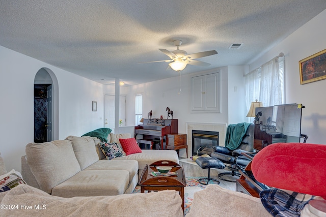 living room featuring hardwood / wood-style flooring, ceiling fan, a tiled fireplace, and a textured ceiling