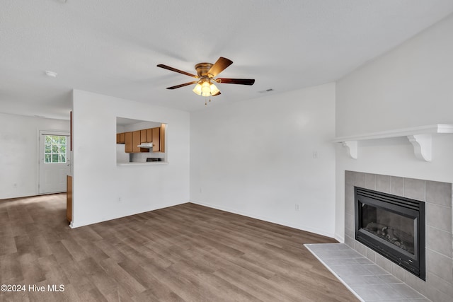 unfurnished living room featuring ceiling fan, light hardwood / wood-style floors, a textured ceiling, and a tiled fireplace