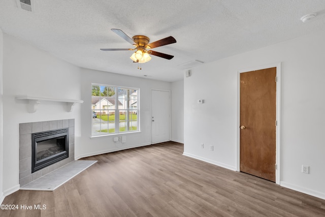 unfurnished living room featuring a tiled fireplace, ceiling fan, light hardwood / wood-style floors, and a textured ceiling