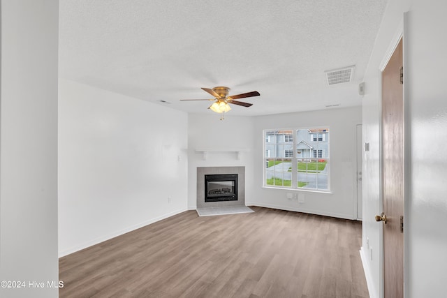 unfurnished living room with a tile fireplace, ceiling fan, light hardwood / wood-style floors, and a textured ceiling