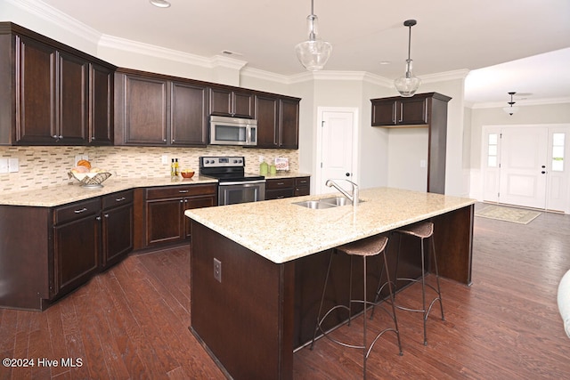 kitchen featuring an island with sink, stainless steel appliances, backsplash, hanging light fixtures, and sink