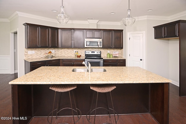 kitchen featuring decorative light fixtures, sink, dark brown cabinetry, appliances with stainless steel finishes, and an island with sink