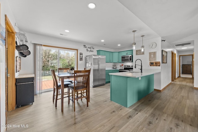 kitchen with a breakfast bar, hanging light fixtures, light hardwood / wood-style flooring, kitchen peninsula, and stainless steel appliances