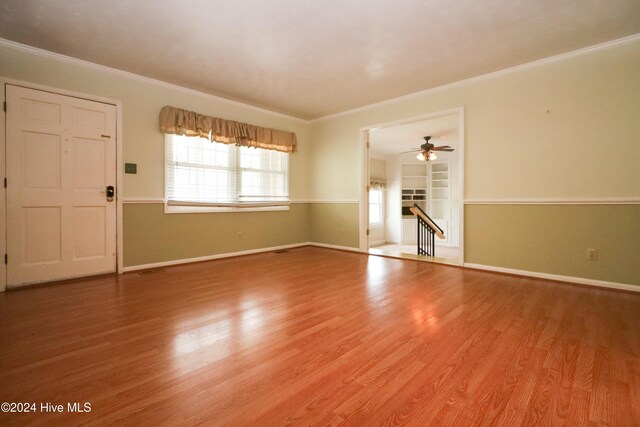 unfurnished living room with built in shelves, ceiling fan, wood-type flooring, and ornamental molding