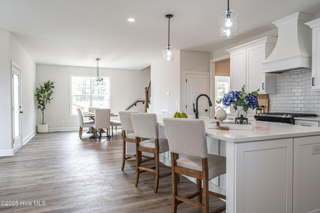 kitchen with stainless steel gas stove, a sink, light stone countertops, premium range hood, and backsplash