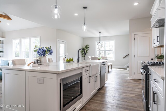 kitchen featuring light stone counters, wood finished floors, baseboards, white cabinets, and a center island with sink