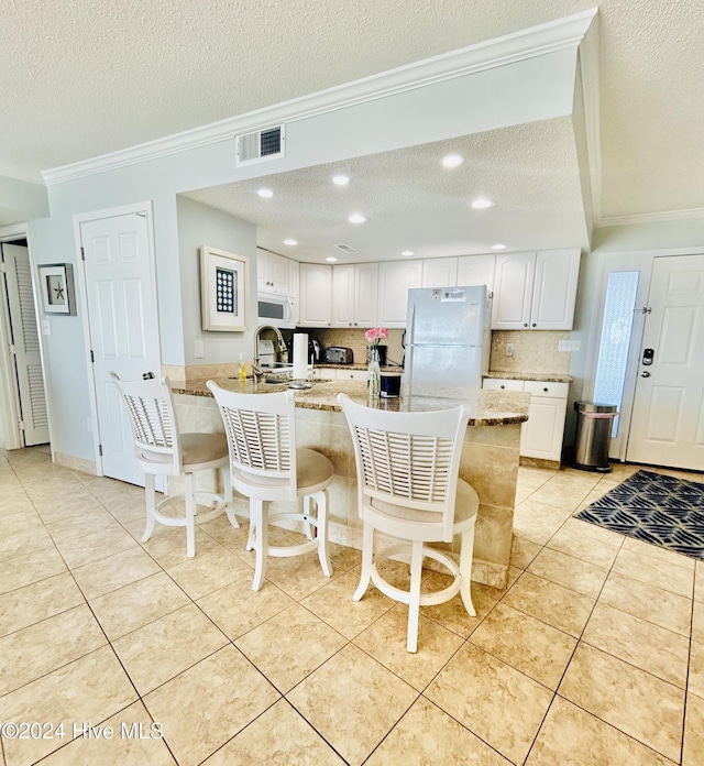 kitchen featuring a kitchen breakfast bar, white appliances, a textured ceiling, light tile patterned floors, and white cabinets