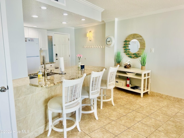 kitchen featuring a kitchen breakfast bar, white refrigerator, sink, light stone counters, and white cabinetry