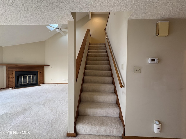 staircase featuring carpet flooring, a textured ceiling, ceiling fan, a fireplace, and lofted ceiling